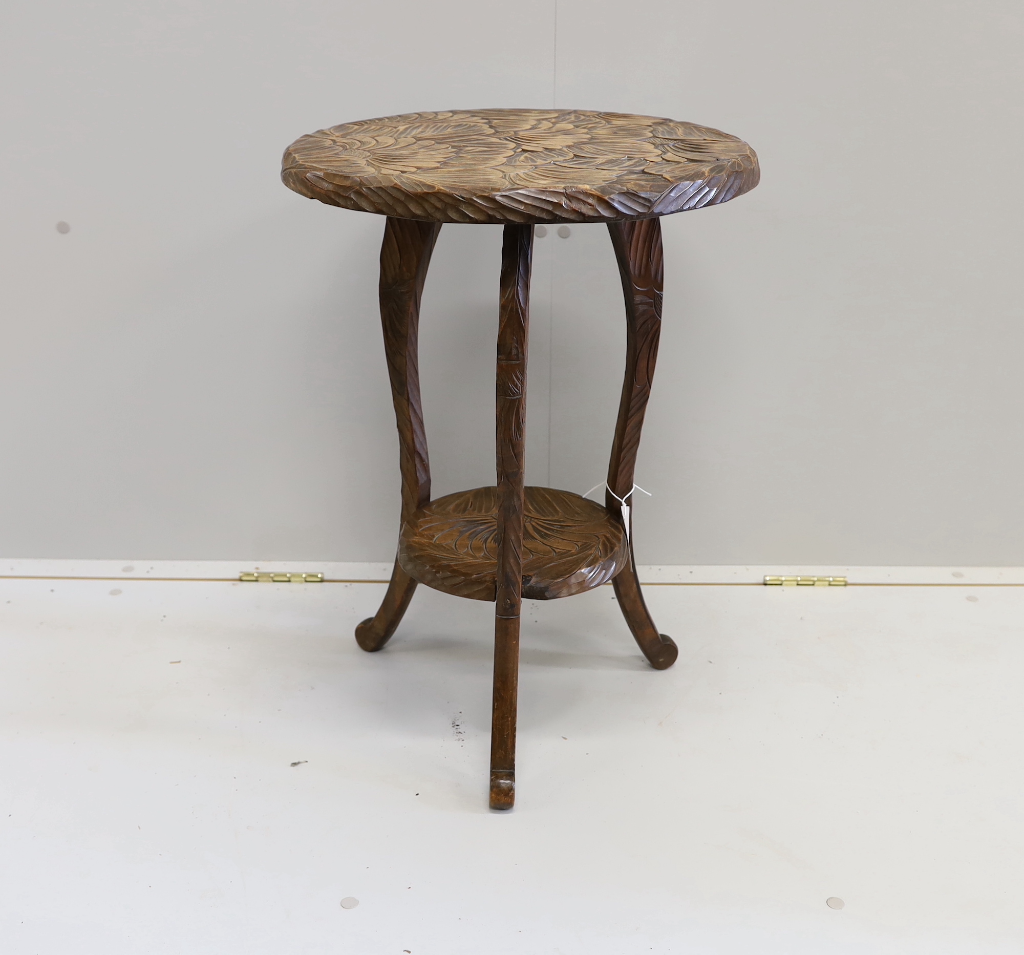 An early 20th century Liberty style carved two tier occasional table, diameter 44cm, height 61cm